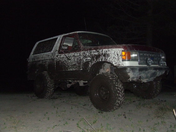 Mud-covered white and maroon SUV, 3/4 front view, with large off-road tires