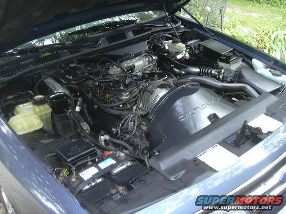 Blue car engine bay with hood open, showing engine components, battery, and coolant reservoirs