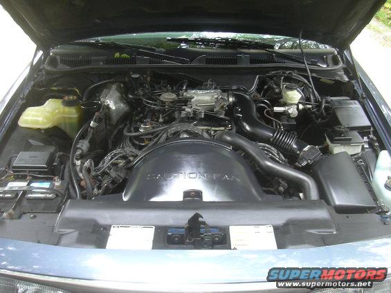 Engine bay with V8 engine, air intake, and coolant reservoir visible. 'CAUTION FAN' is written on the fan shroud