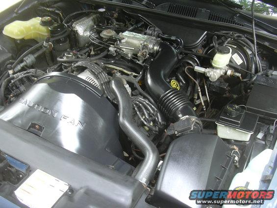 Engine bay of a 1996 Ford Crown Victoria. Shows the air intake, fan shroud, and brake fluid reservoir