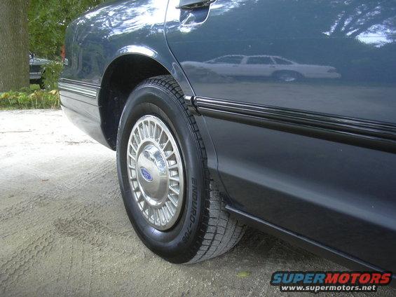 1996 Ford Crown Victoria side view, dark blue sedan rear quarter panel and wheel with chrome hubcap