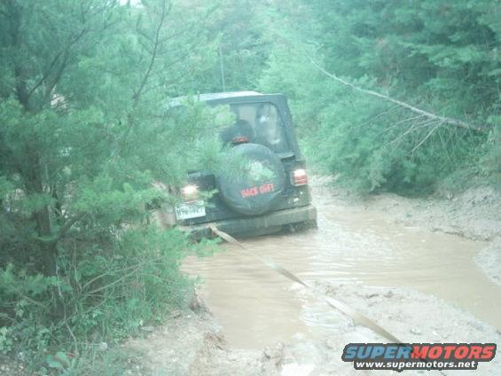 2003 Jeep Wrangler driving through a muddy trail with trees on the side