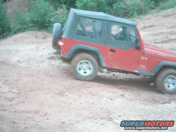 Red Jeep Wrangler with soft top driving on a dirt trail