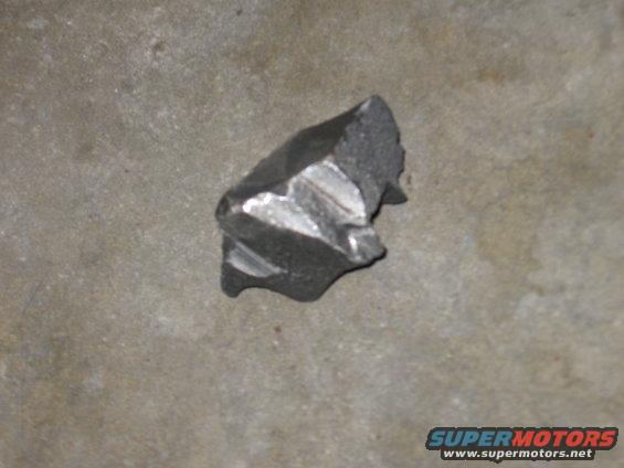 Fragment of a dark metal part with machined grooves, lying on a concrete surface