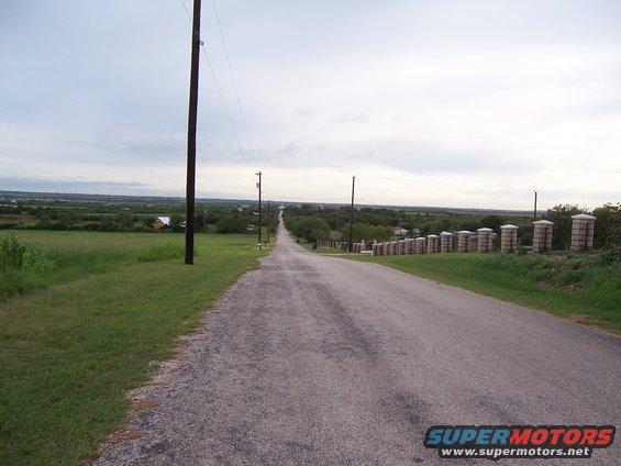 Long asphalt road with grassy fields and telephone poles under a cloudy sky