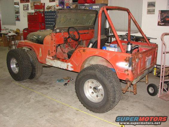 Orange Jeep CJ5 with roll cage and large tires, in a garage