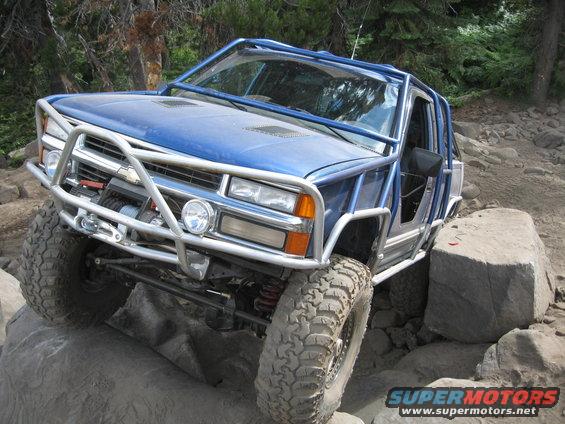 Blue 1997 Chevrolet C/K Pickup modified for off-roading, with a roll cage and winch, climbing over large rocks
