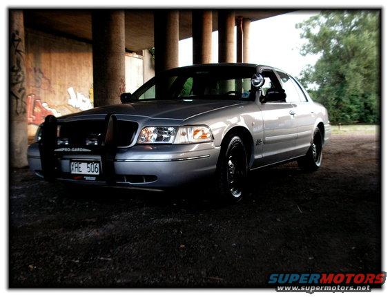 Silver police car with push bar and black wheels parked under an overpass