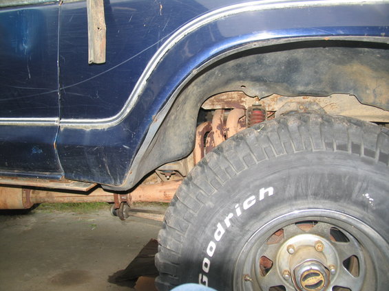 Close-up of a blue vehicle's rear wheel well, showing the tire, suspension components, and exhaust pipe