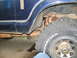 1978 Ford Bronco - Close-up view of a blue vehicle's side, showing the fender, tire, and undercarriage components.
