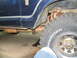 1978 Ford Bronco - Close-up view of the side of a blue vehicle, showing the tire, exhaust, and suspension components.