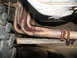 1978 Ford Bronco - Close-up view of rusty exhaust headers and pipe underneath a vehicle.