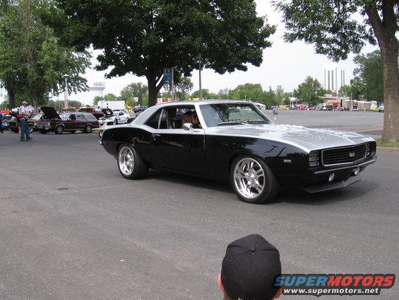 Black and silver 1969 Chevrolet Camaro SS driving on pavement, other cars in background