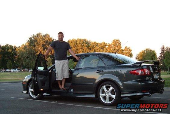 Man standing with driver's door open on a dark gray 2005 Mazda 6 sedan with a rear spoiler