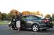 2005 Mazda 6 - A man leans on the open door of a dark gray 2005 Mazda 6 sedan with a rear spoiler.