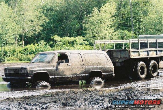 Muddy SUV towing a trailer through a muddy track. The SUV appears to be from the 1980s