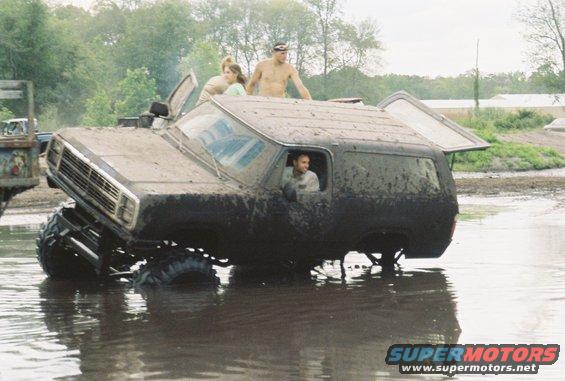Mud-covered SUV stuck in water, front end lifted, people on top and inside