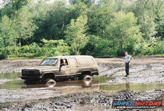 Muddy 1991 Chevrolet Suburban stuck in a muddy puddle with a person standing nearby