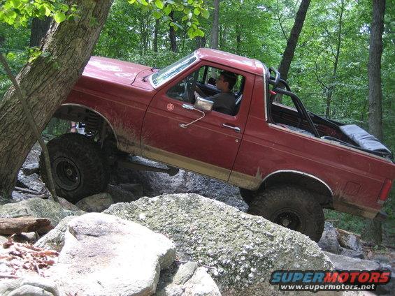 Red 1990 Ford Bronco navigating a rocky trail, angled to the front