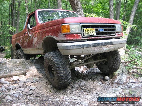 Red 1990 Ford Bronco on rocky trail, front 3/4 view