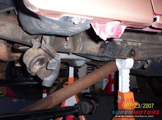Undercarriage of a vehicle on jack stands, showing brake caliper and suspension components