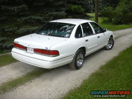 White 1997 Ford Crown Victoria sedan, rear 3/4 view, chrome wheels, on a gravel driveway
