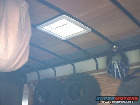 Trailer interior showing a roof vent, large tires, and a helmet hanging on the wall