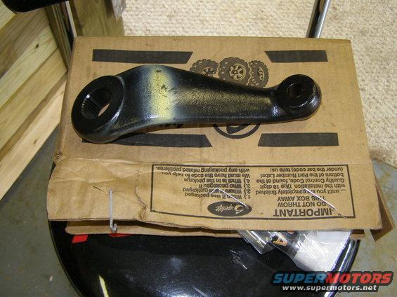 Black steering linkage part with yellow markings on a cardboard box