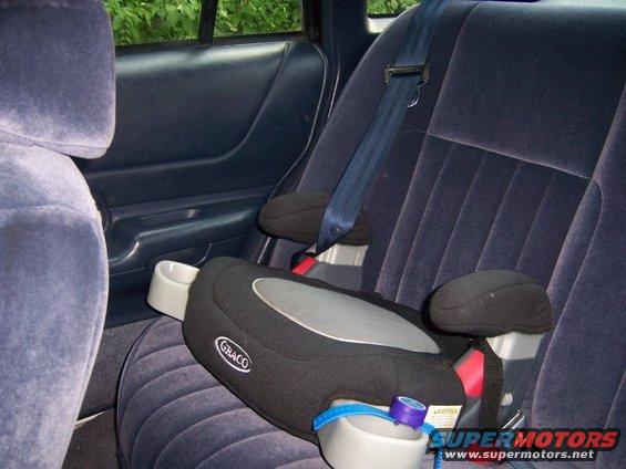 Child booster seat on dark blue velour rear car seat, with cup holders and seatbelt visible