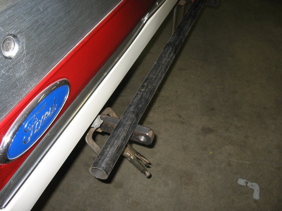 Close-up of a blue Ford oval emblem on a red and silver vehicle panel, with a metal pipe clamped to it