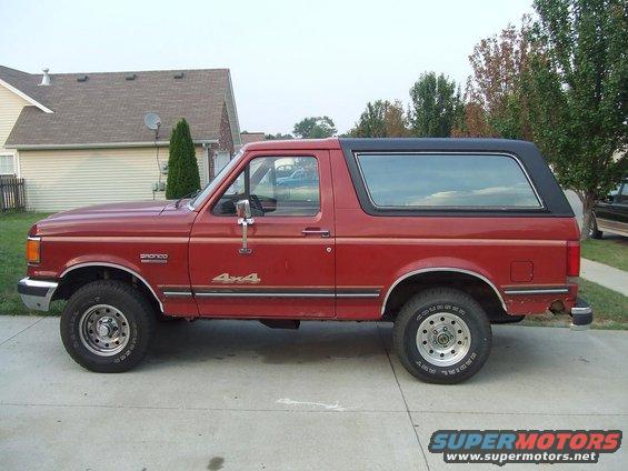 Red 1987 Ford Bronco side view with black top and 4x4 badging