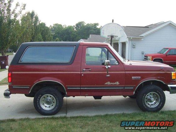 Red 1987 Ford Bronco 4x4 SUV, side view, black removable top, chrome wheels, parked on driveway