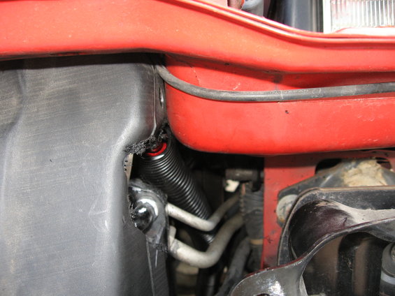 Red vehicle fender with black corrugated tubing and silver hoses visible in the engine bay