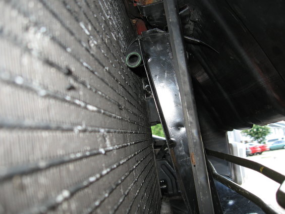 close-up of car radiator fins and black fan shroud with some hoses