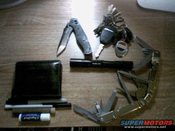 Wallet, pocket knife, flashlight, keys, and multi-tool laid out on a wooden surface