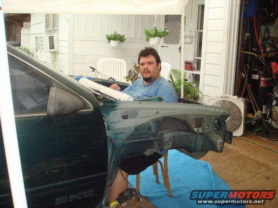 Disassembled dark green car fender and door panel with a man sitting inside