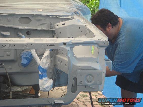 Car engine bay being prepped for paint, with blue tarp in background