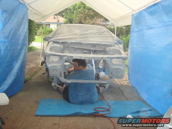 Car chassis covered in plastic, being worked on by a person in a blue shirt inside a tent