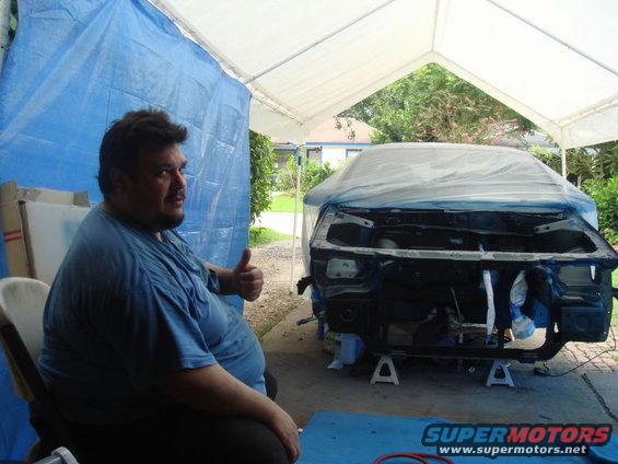 Man in blue shirt gives thumbs up next to a car with its front end disassembled and covered