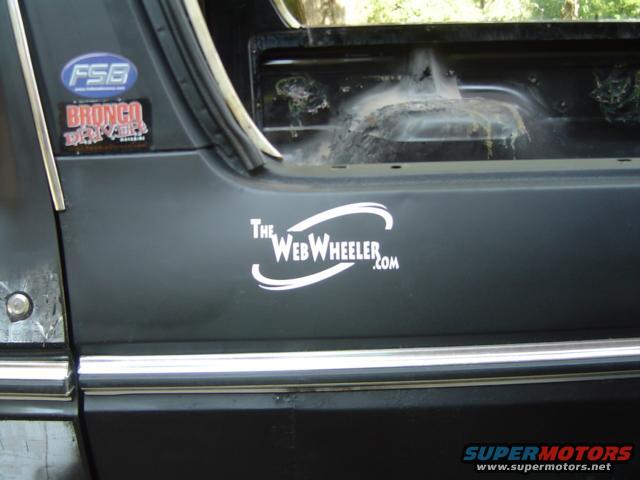 Side of a dark vehicle with "The WebWheeler.com" sticker and a "Bronco" sticker