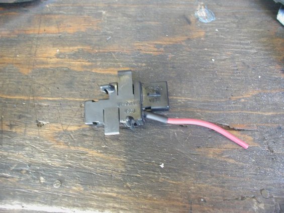 Automotive electrical connector with a red wire attached, resting on a wooden surface. Text on the part reads 'SF-9301A 9963'