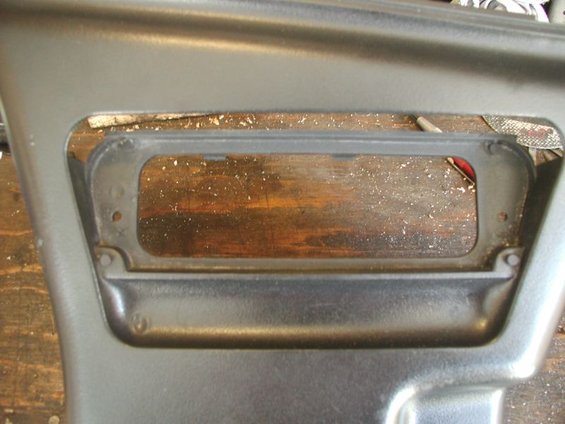 Close-up of a dark gray plastic car interior panel with a rectangular cutout showing a wooden surface and some debris