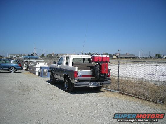 Two-tone gray and white 1991 Ford Bronco with red storage boxes and spare tire mounted on the rear
