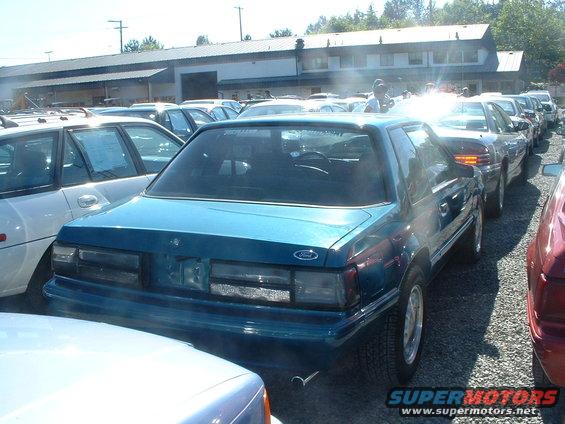 Teal Ford Mustang coupe, rear view, parked in a lot with other cars