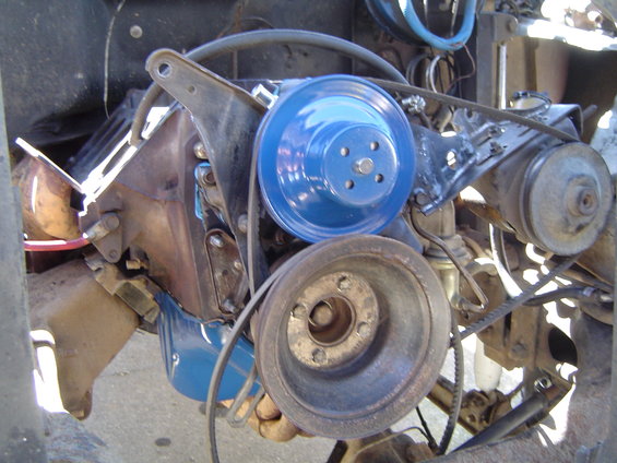 Engine pulleys and belts, one blue, one rusty, with metal brackets and engine block visible