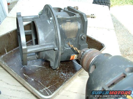 Drill bit entering a metal carburetor body sitting in a metal tray