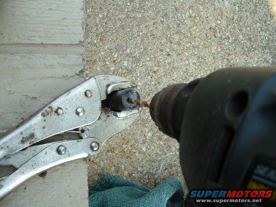 Drill bit entering a cylindrical part held by vise grips. A blue towel is visible below