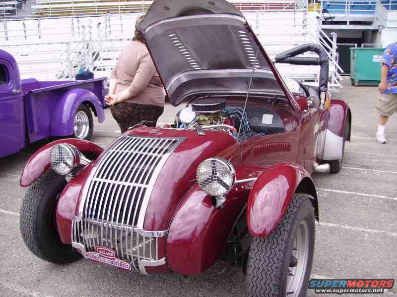 Red roadster with hood open, parked next to a purple pickup truck