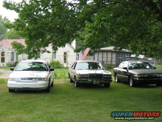Three sedans parked on grass, one is a 1988 Mercury Grand Marquis with a chrome grille