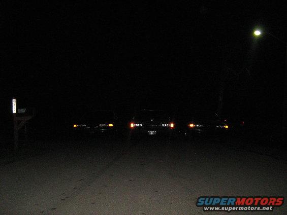three cars parked on a dark road at night, headlights on